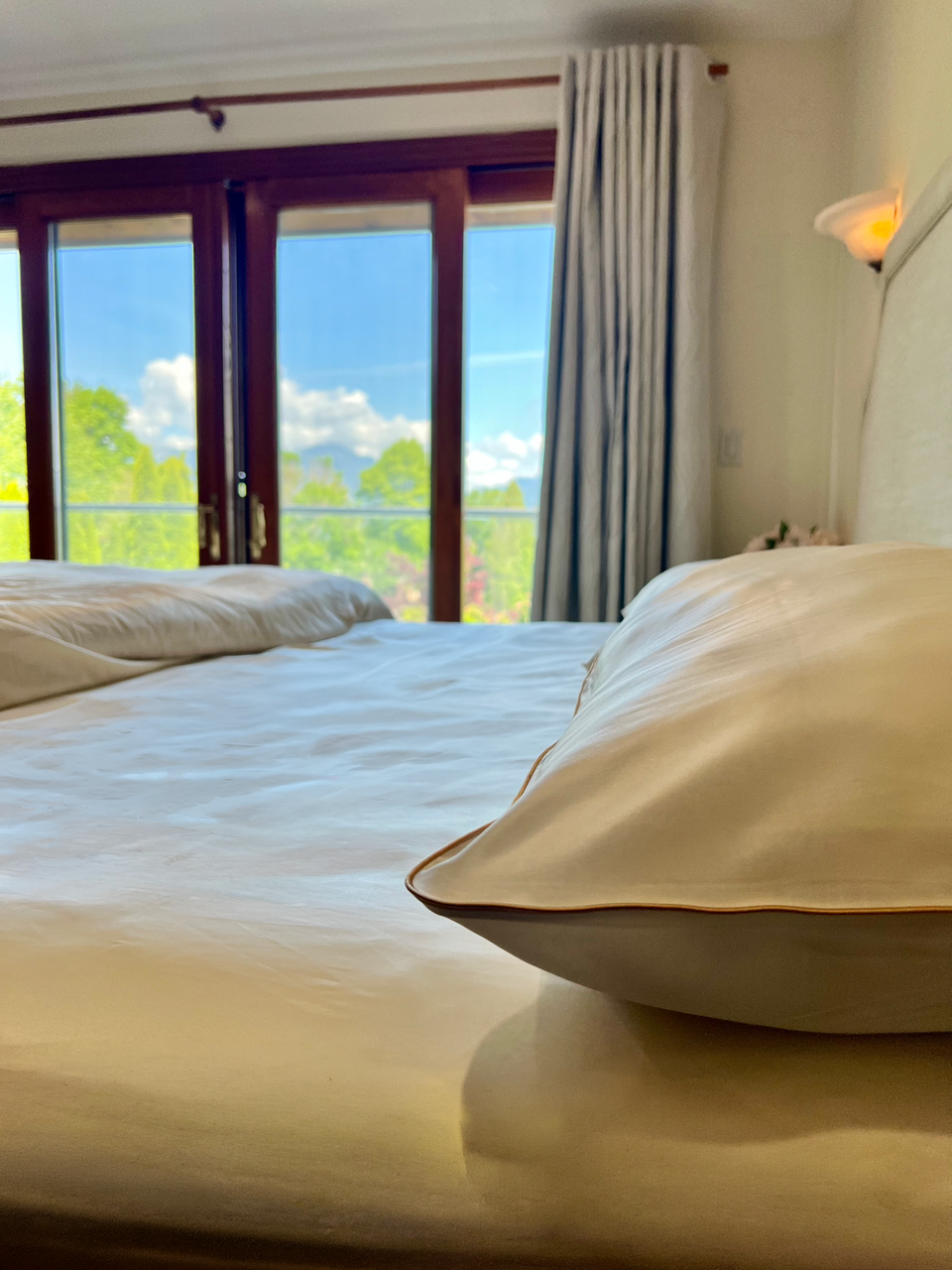 Ivory-gold silk pillowcase and bedding set on a bed, with patio doors and a hillside view behind